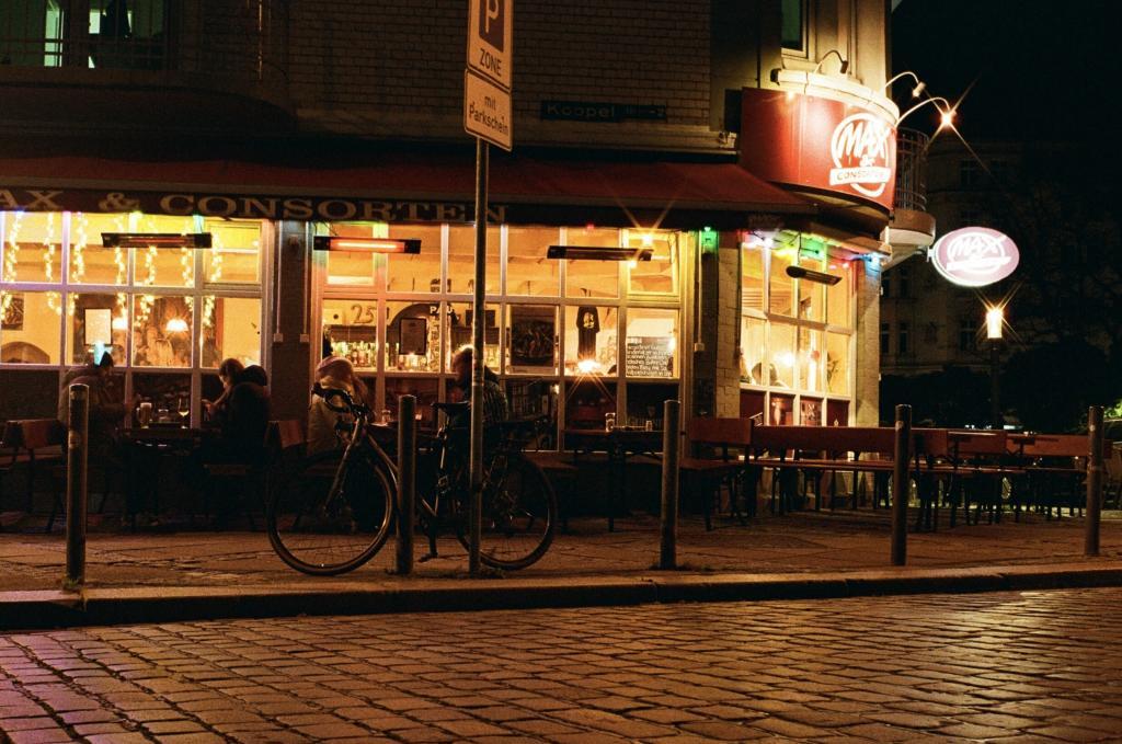 In einer dunklen Straße sieht man von außen durch die Fenster eines Cafe - das Licht spiegelt sich auf dem Kopfsteinpflaster.